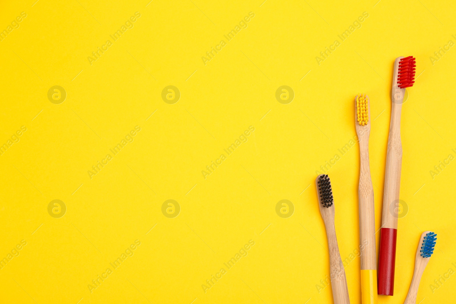 Photo of Toothbrushes made of bamboo on yellow background, flat lay. Space for text