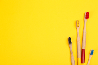 Photo of Toothbrushes made of bamboo on yellow background, flat lay. Space for text