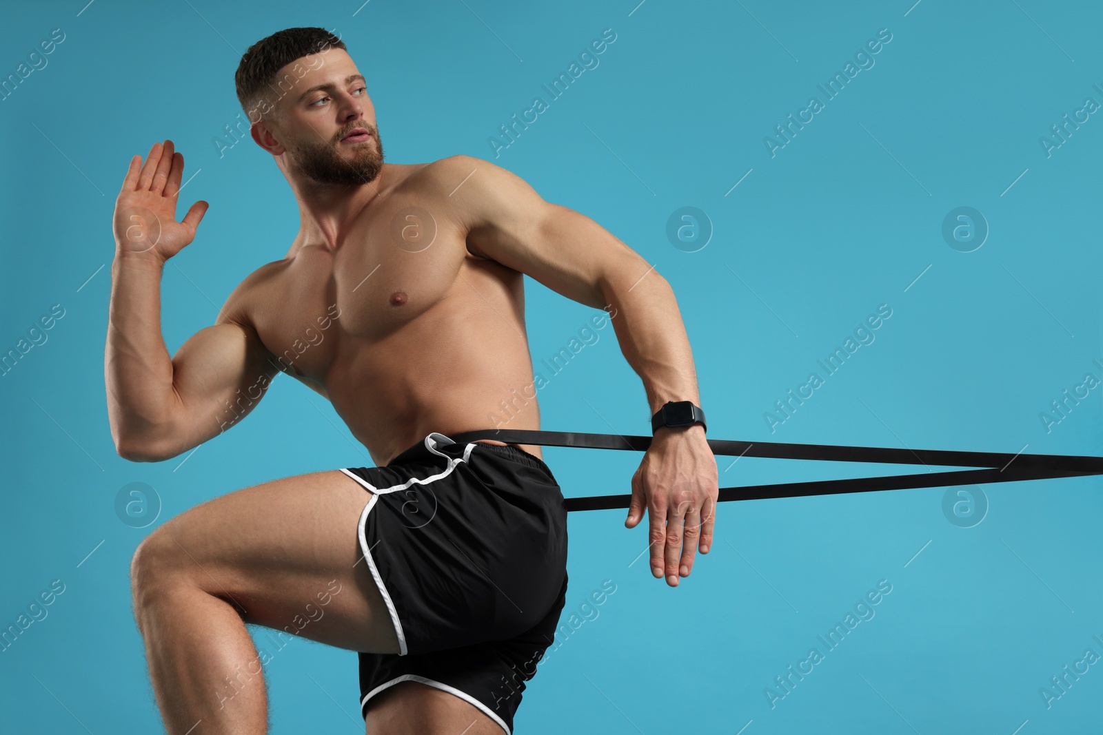 Photo of Muscular man exercising with elastic resistance band on light blue background