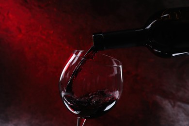 Pouring red wine from bottle into glass on color background, closeup