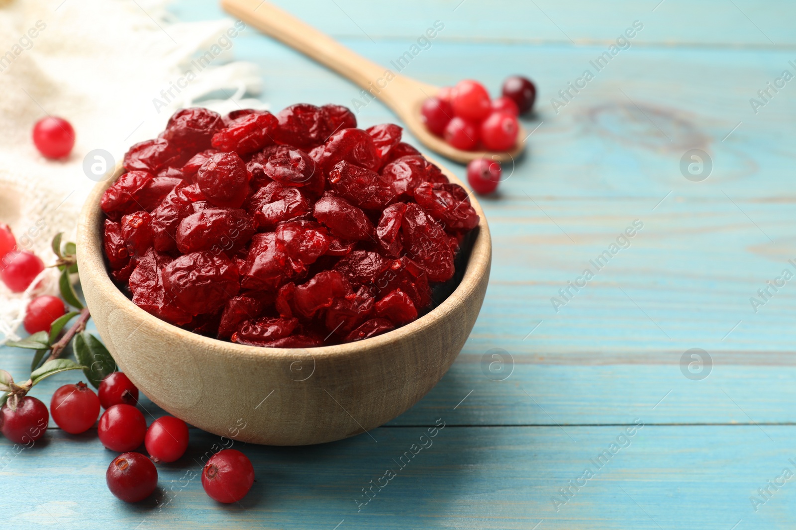 Photo of Tasty dried cranberries in bowl and fresh ones on light blue wooden table, closeup. Space for text