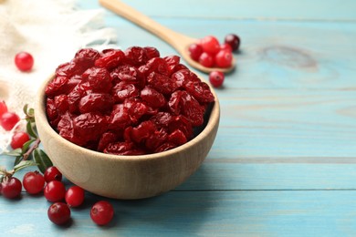 Photo of Tasty dried cranberries in bowl and fresh ones on light blue wooden table, closeup. Space for text