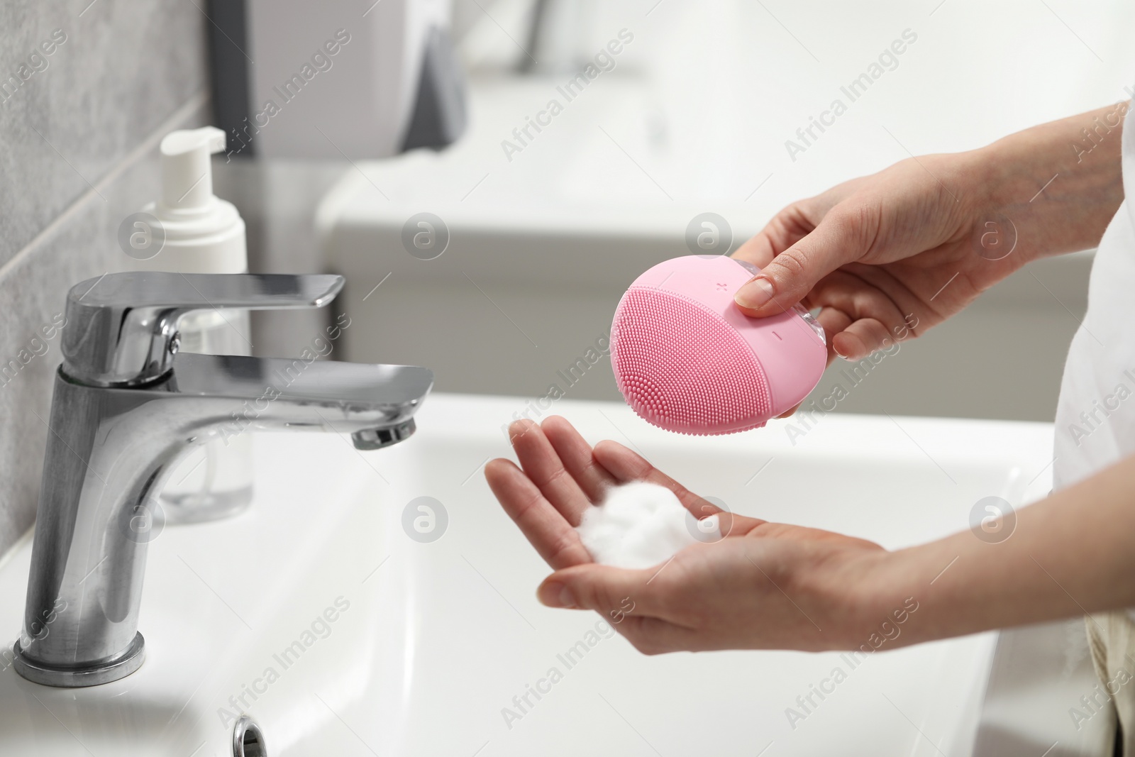 Photo of Washing face. Woman with brush and cleansing foam above sink in bathroom, closeup