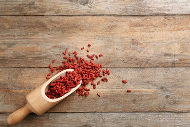Scoop and dried goji berries on wooden table, top view with space for text. Healthy superfood