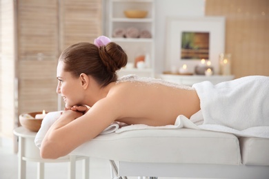 Beautiful young woman having massage with body scrub in spa salon