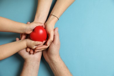 Parents and child holding red decorative heart on light blue background, top view. Space for text