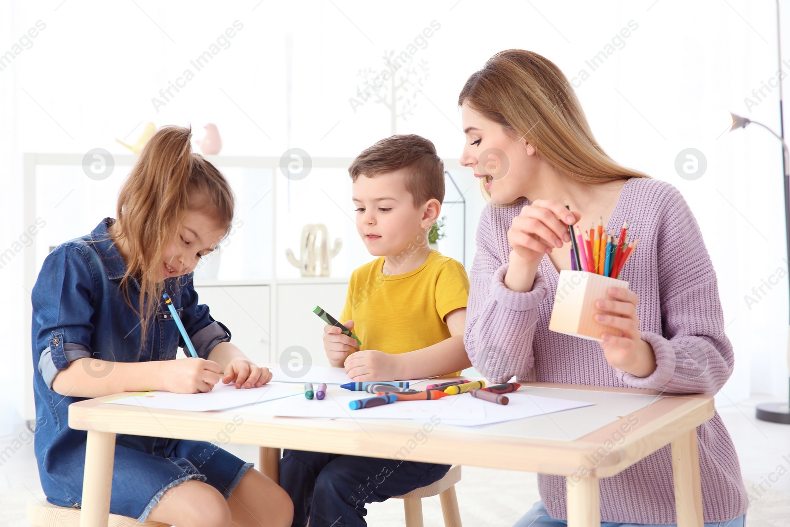 Photo of Cute little children and their nanny drawing at home