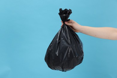 Photo of Woman holding plastic bag full of garbage on light blue background, closeup. Space for text