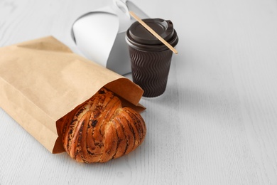 Photo of Paper bag with pastry and takeaway food on wooden table. Space for text