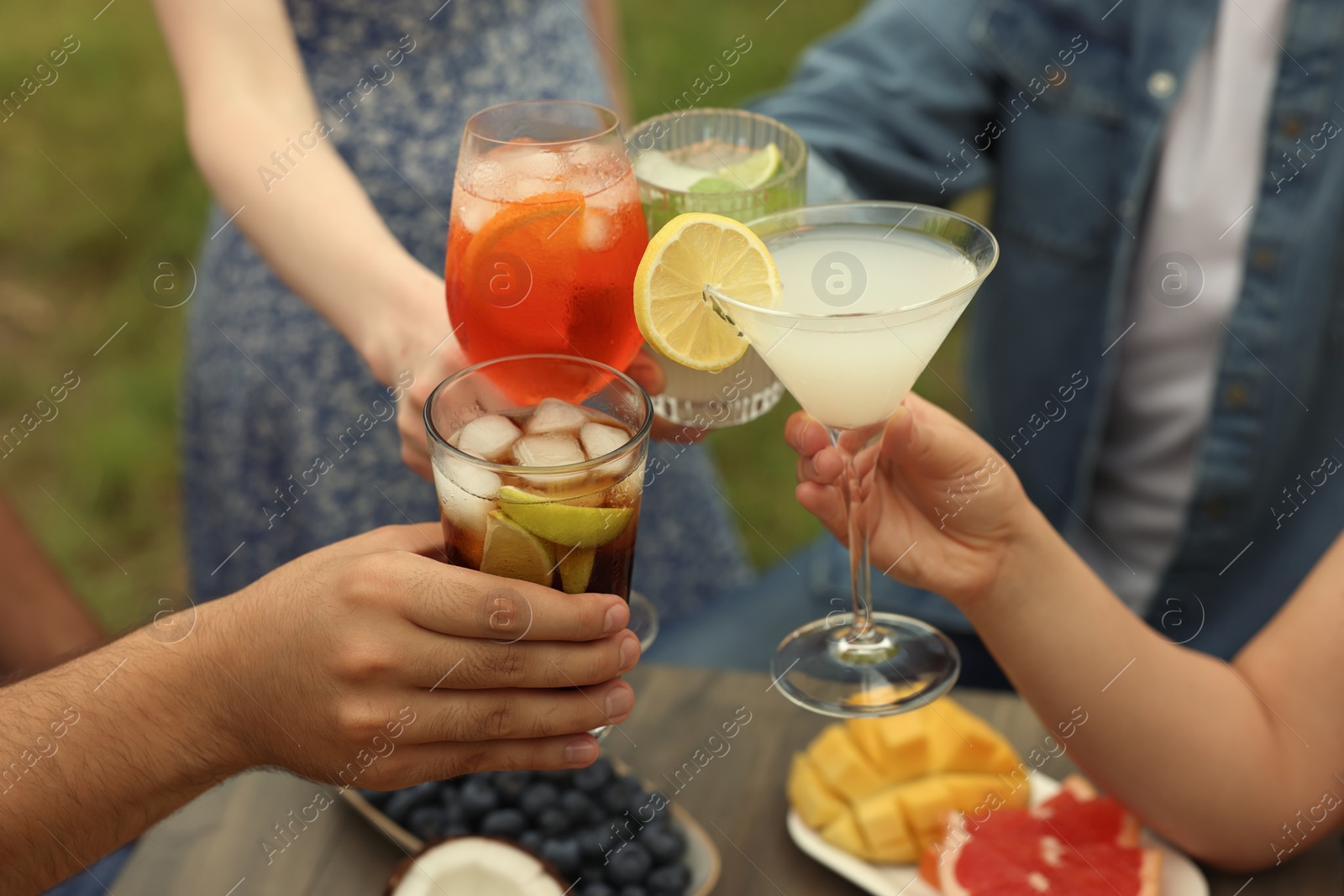 Photo of Friends clinking glasses with cocktails at table outdoors, closeup