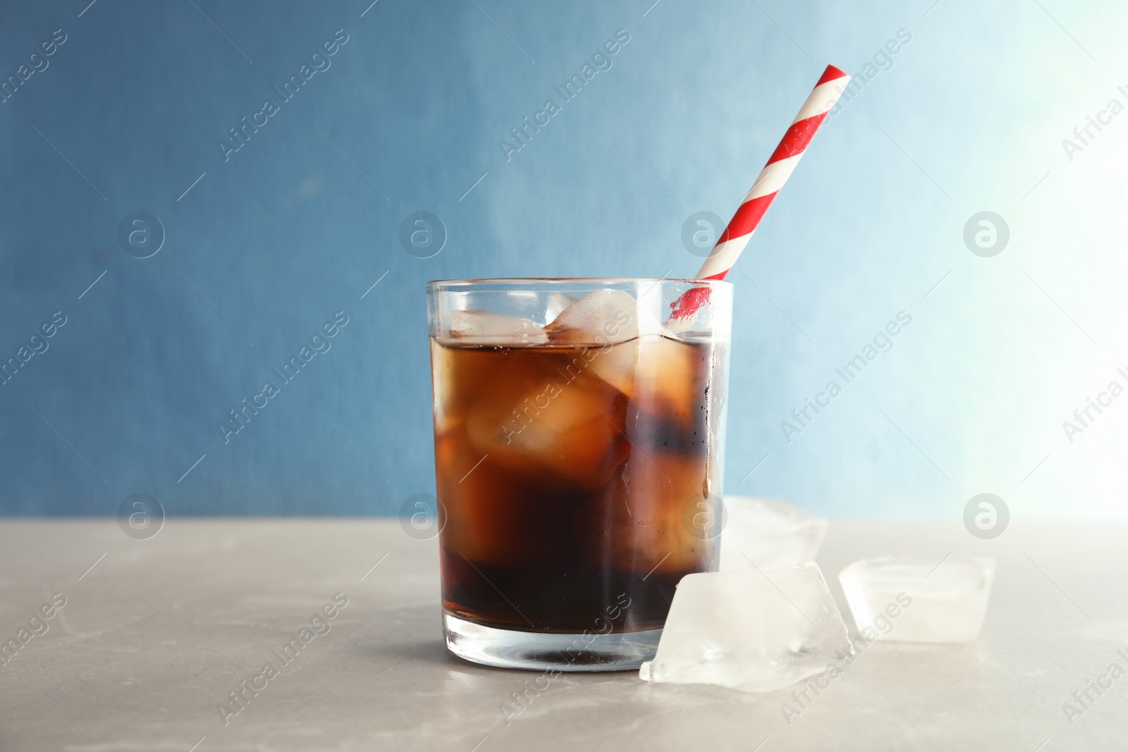 Photo of Glass of refreshing cola with ice on table against color background