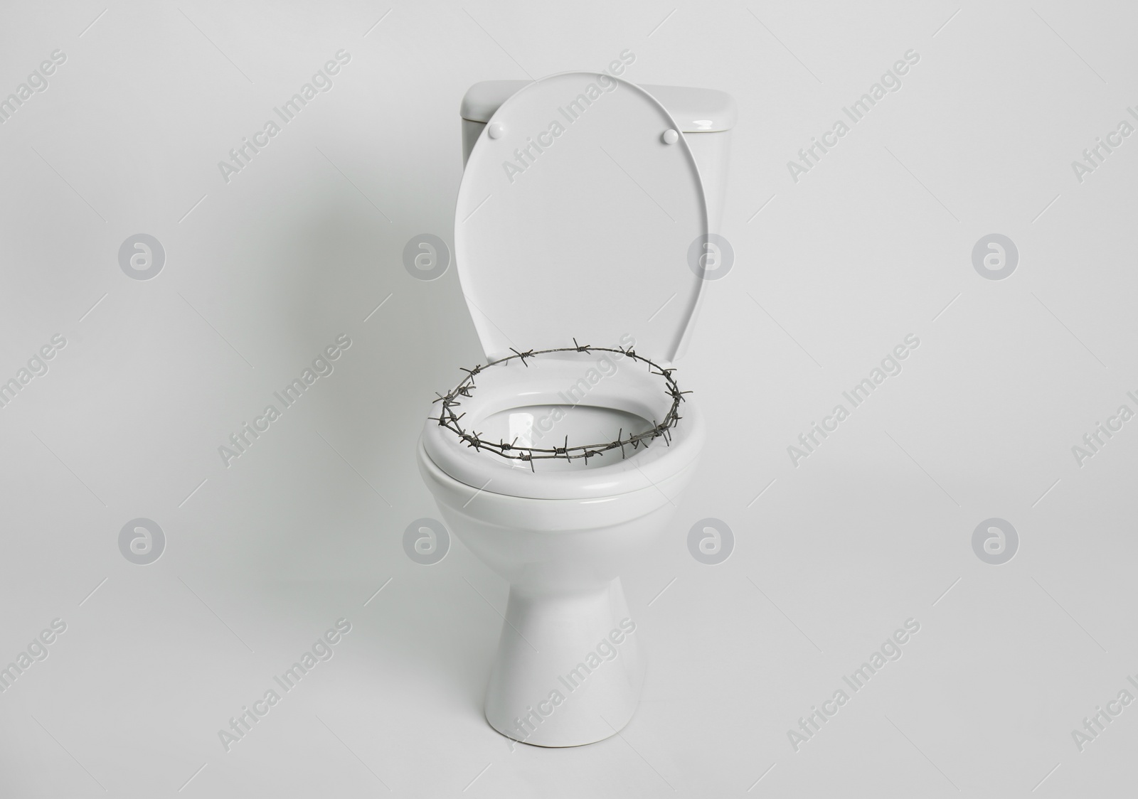 Photo of Toilet bowl with barbed wire on white background. Hemorrhoids concept