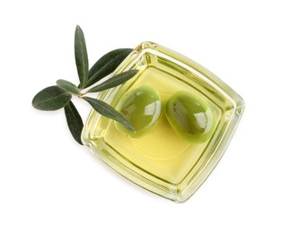 Photo of Glass bowl of oil, ripe olives and green leaves on white background, top view