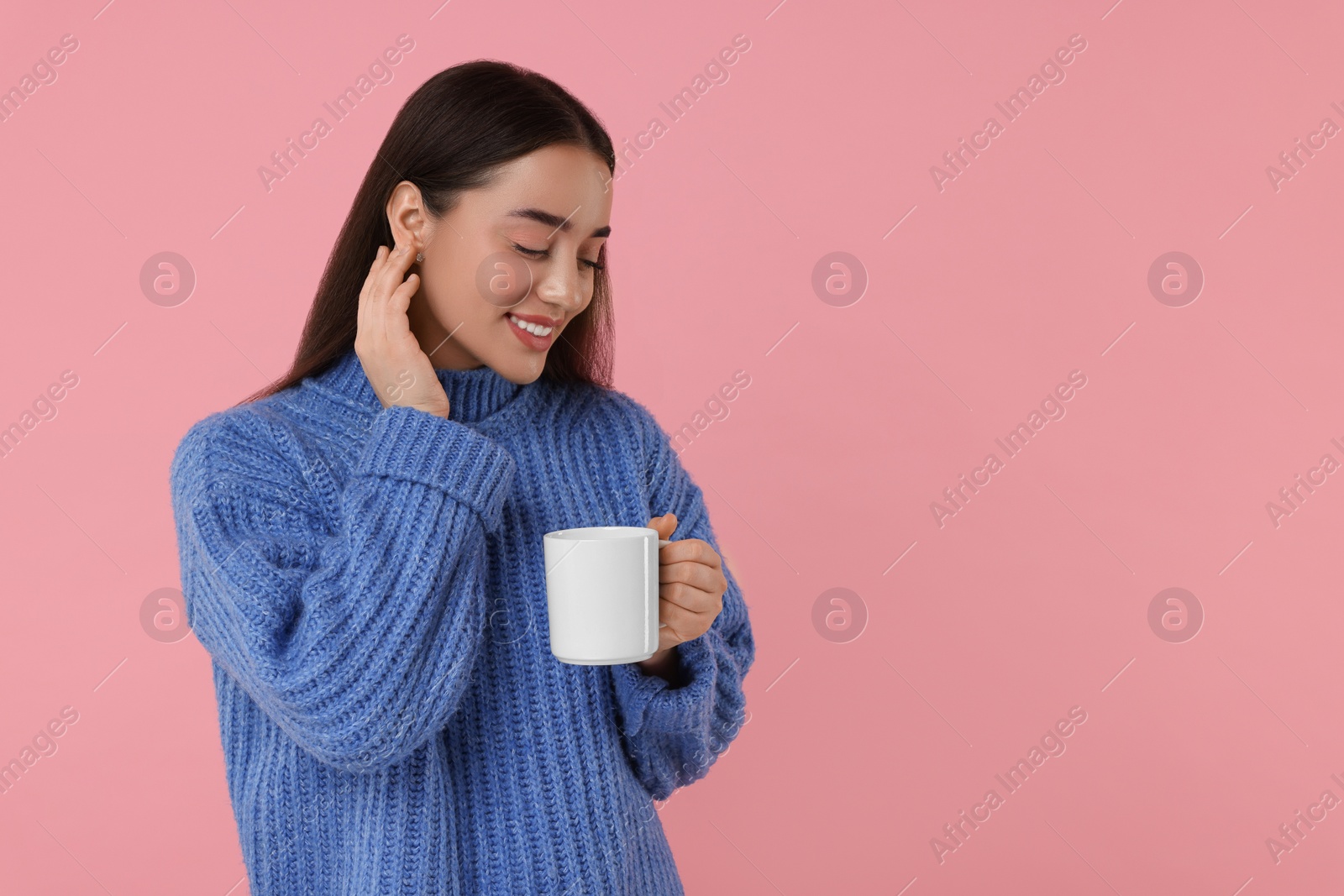 Photo of Happy young woman holding white ceramic mug on pink background, space for text