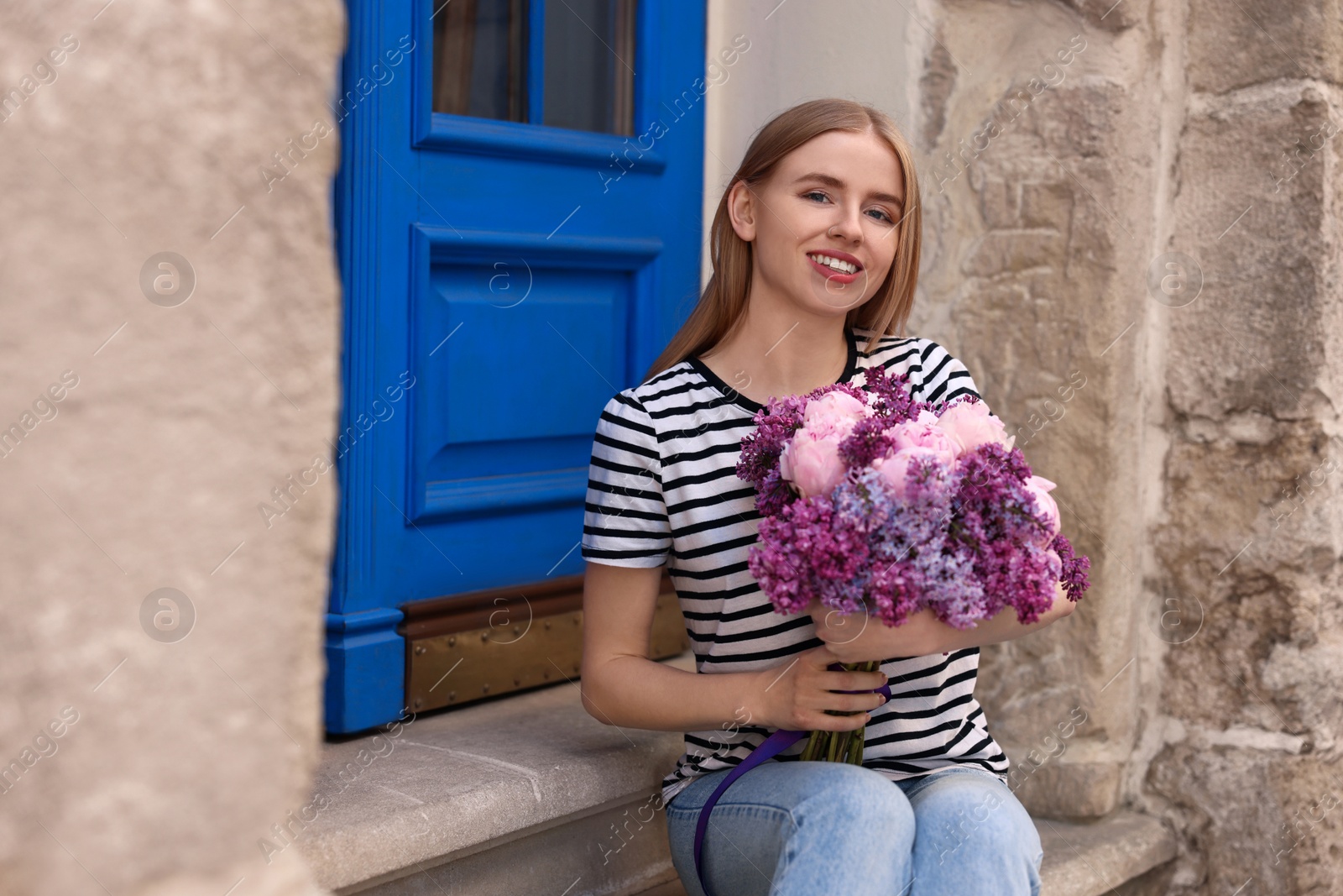 Photo of Beautiful woman with bouquet of spring flowers near building outdoors, space for text