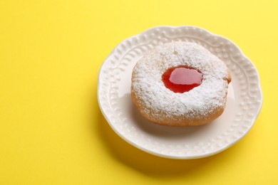Photo of Hanukkah donut with jelly and powdered sugar on yellow background, space for text