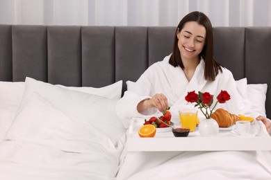 Smiling woman having breakfast in bed at home, space for text