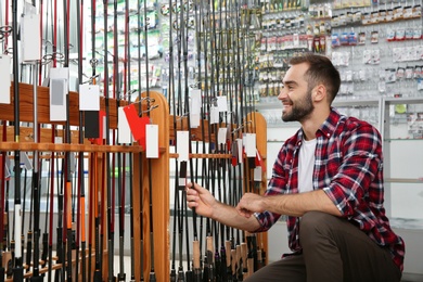 Man choosing fishing rod in sports shop. Space for text