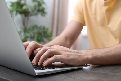 Photo of Young man working with laptop at desk in home office, closeup