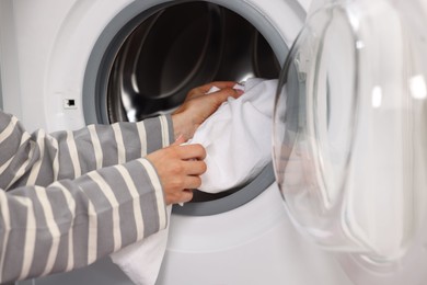 Photo of Woman putting laundry into washing machine indoors, closeup