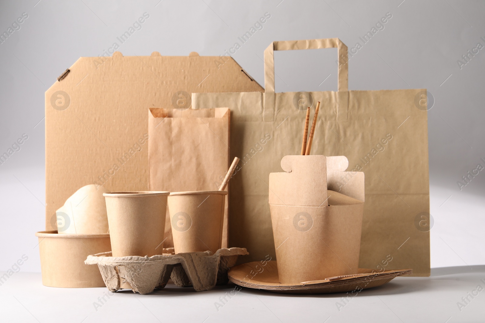 Photo of Eco friendly food packaging. Paper containers, tableware and bag on light background