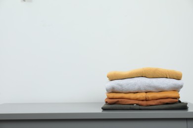 Photo of Sorting and organizing. Stack of different folded clothes on table near white wall, space for text