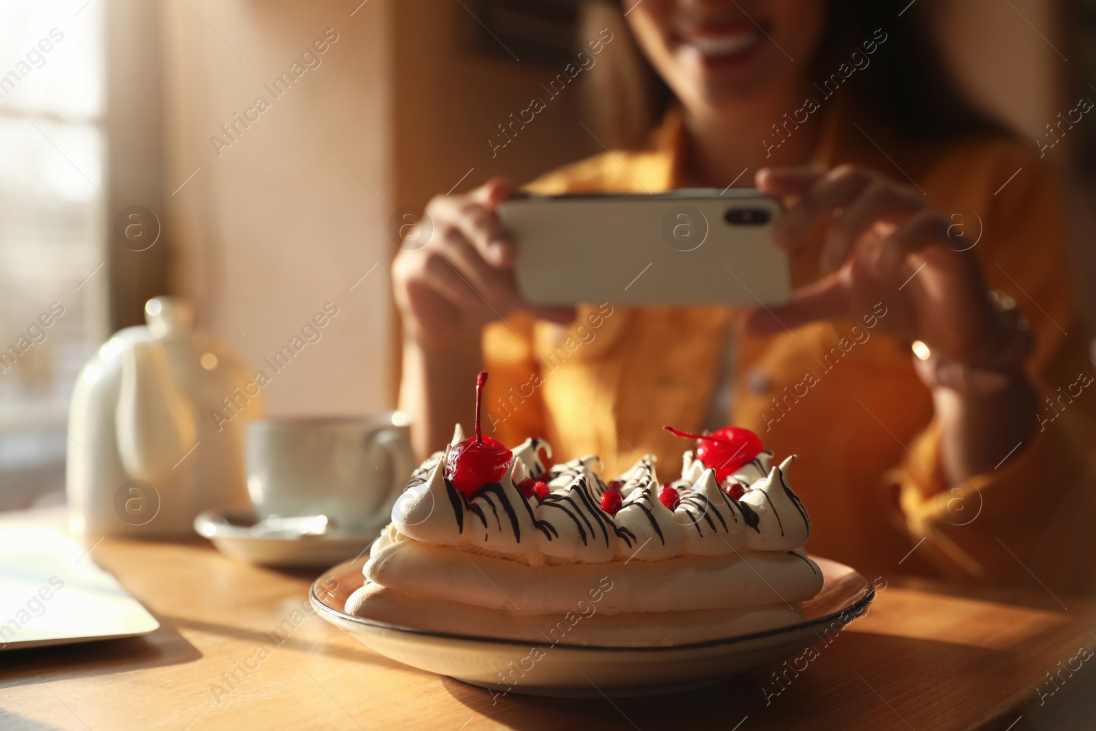 Photo of Young blogger taking picture of dessert at table in cafe, focus on plate