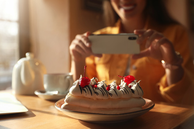 Photo of Young blogger taking picture of dessert at table in cafe, focus on plate