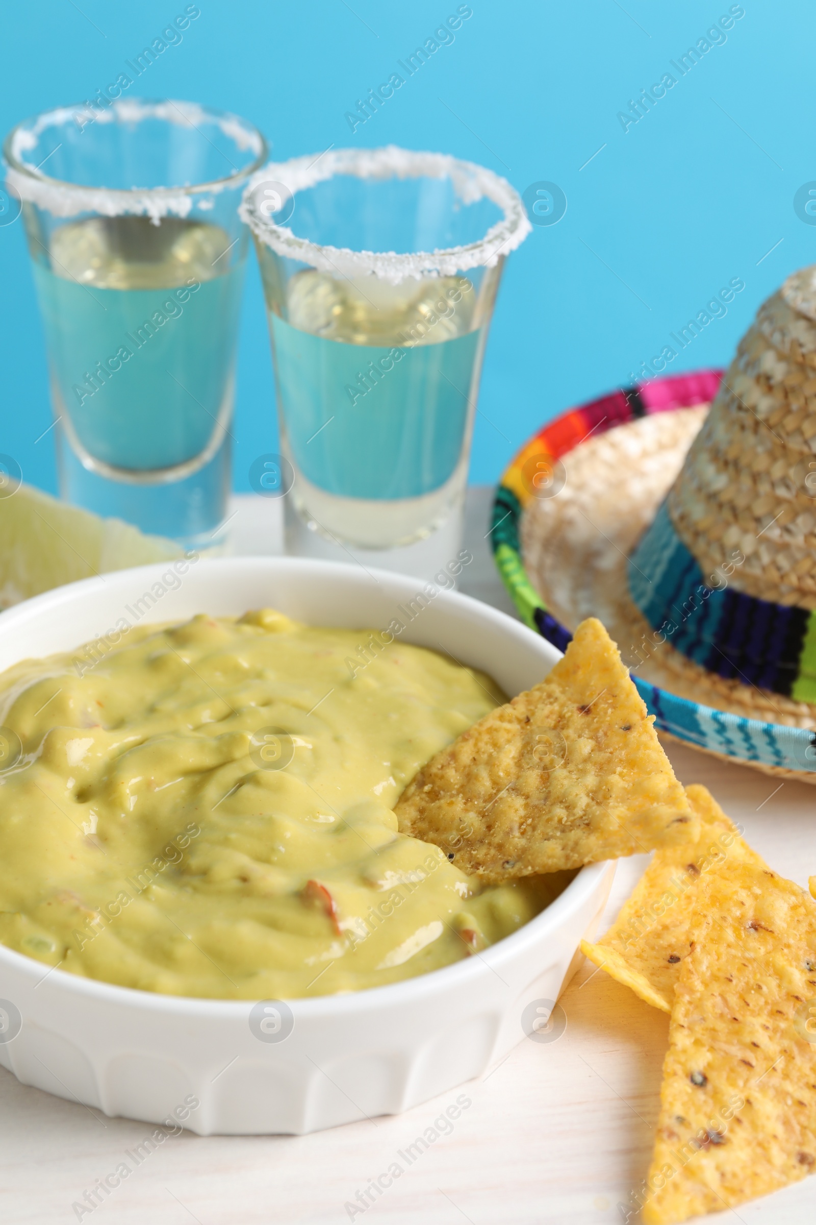 Photo of Delicious guacamole with nachos chips, Mexican sombrero hat and tequila on white wooden table