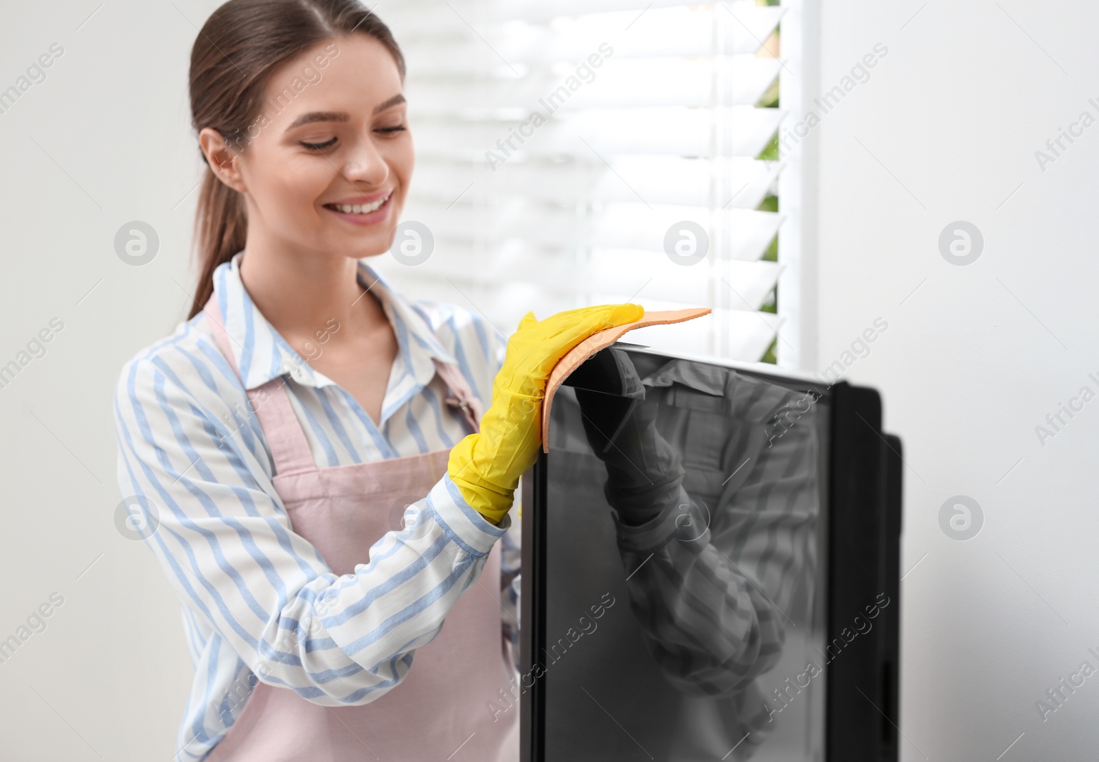 Photo of Young chambermaid wiping dust from TV with rag in hotel room