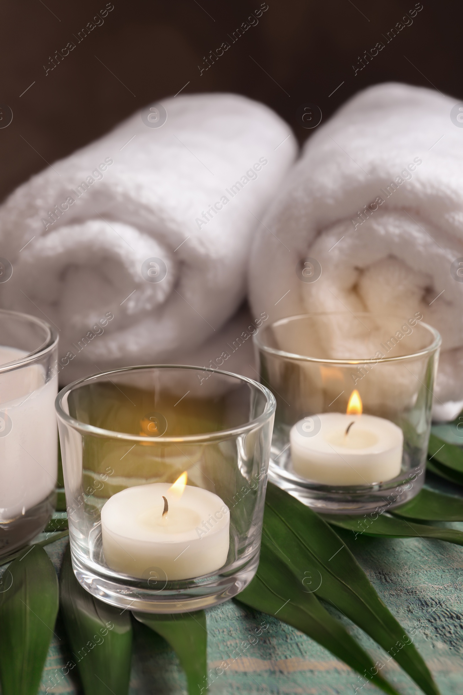 Photo of Spa composition with burning wax candles, towels and tropical leaf on table