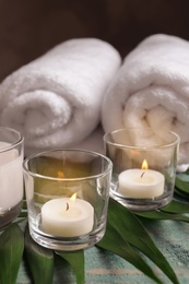 Photo of Spa composition with burning wax candles, towels and tropical leaf on table