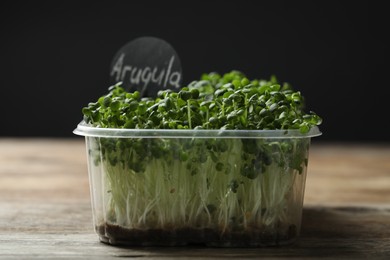 Photo of Sprouted arugula seeds in plastic container on wooden table
