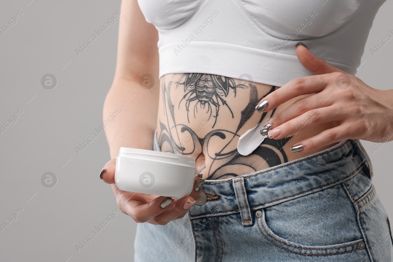 Photo of Woman applying healing cream onto her tattoos against grey background, closeup