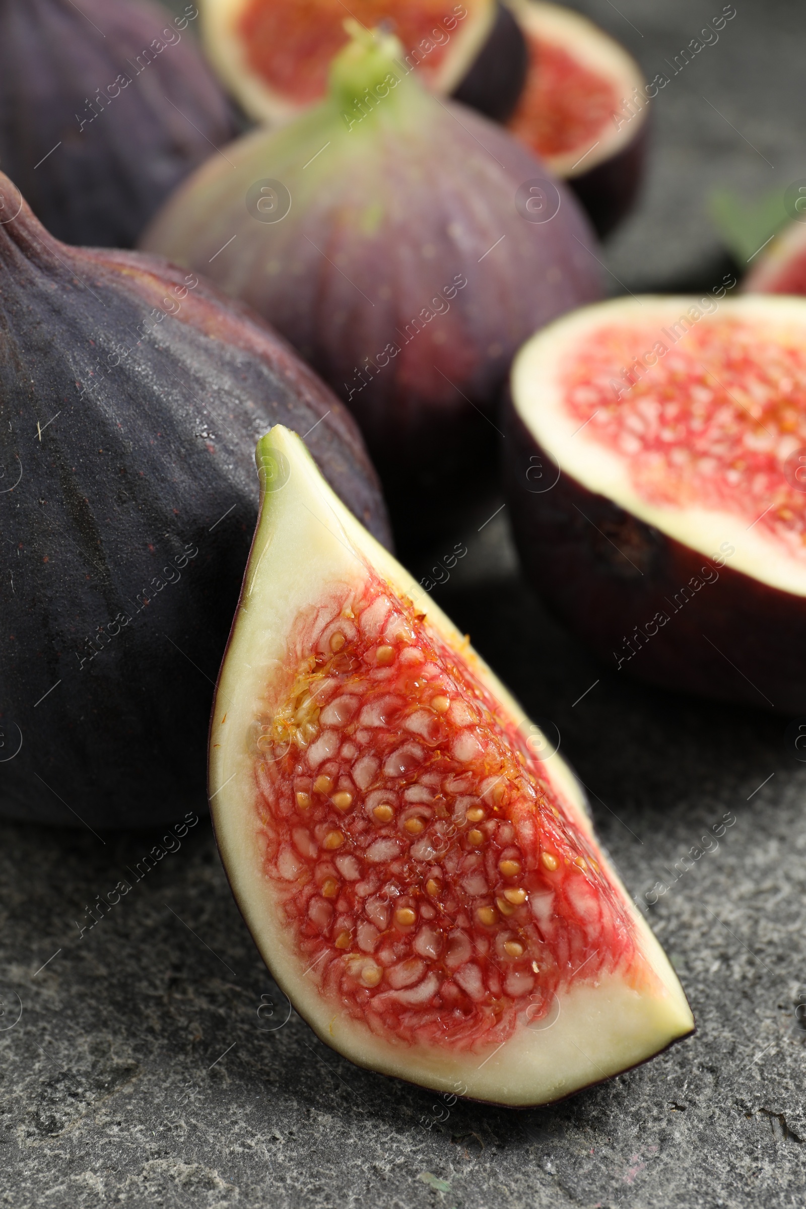 Photo of Whole and cut ripe figs on grey textured table, closeup