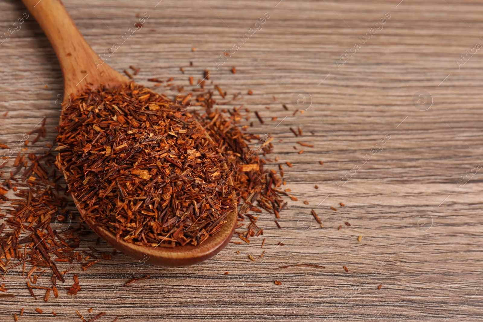 Photo of Spoon with dry rooibos leaves on wooden table, closeup. Space for text