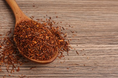 Photo of Spoon with dry rooibos leaves on wooden table, closeup. Space for text