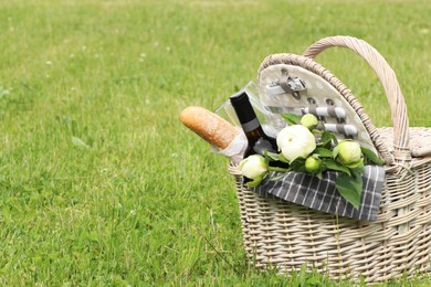 Picnic basket with wine, bread and flowers on green grass outdoors