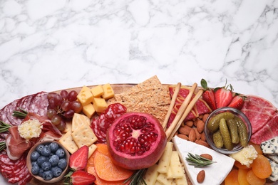 Photo of Wooden plate with different delicious snacks on white marble table, top view. Space for text