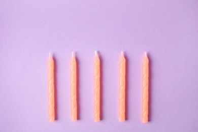 Photo of Orange birthday candles on lilac background, top view