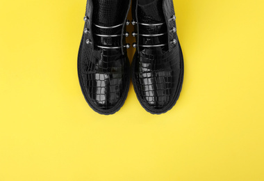 Pair of stylish ankle boots on yellow background, top view. Space for text