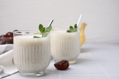 Glasses of delicious date smoothie with mint on white table. Space for text