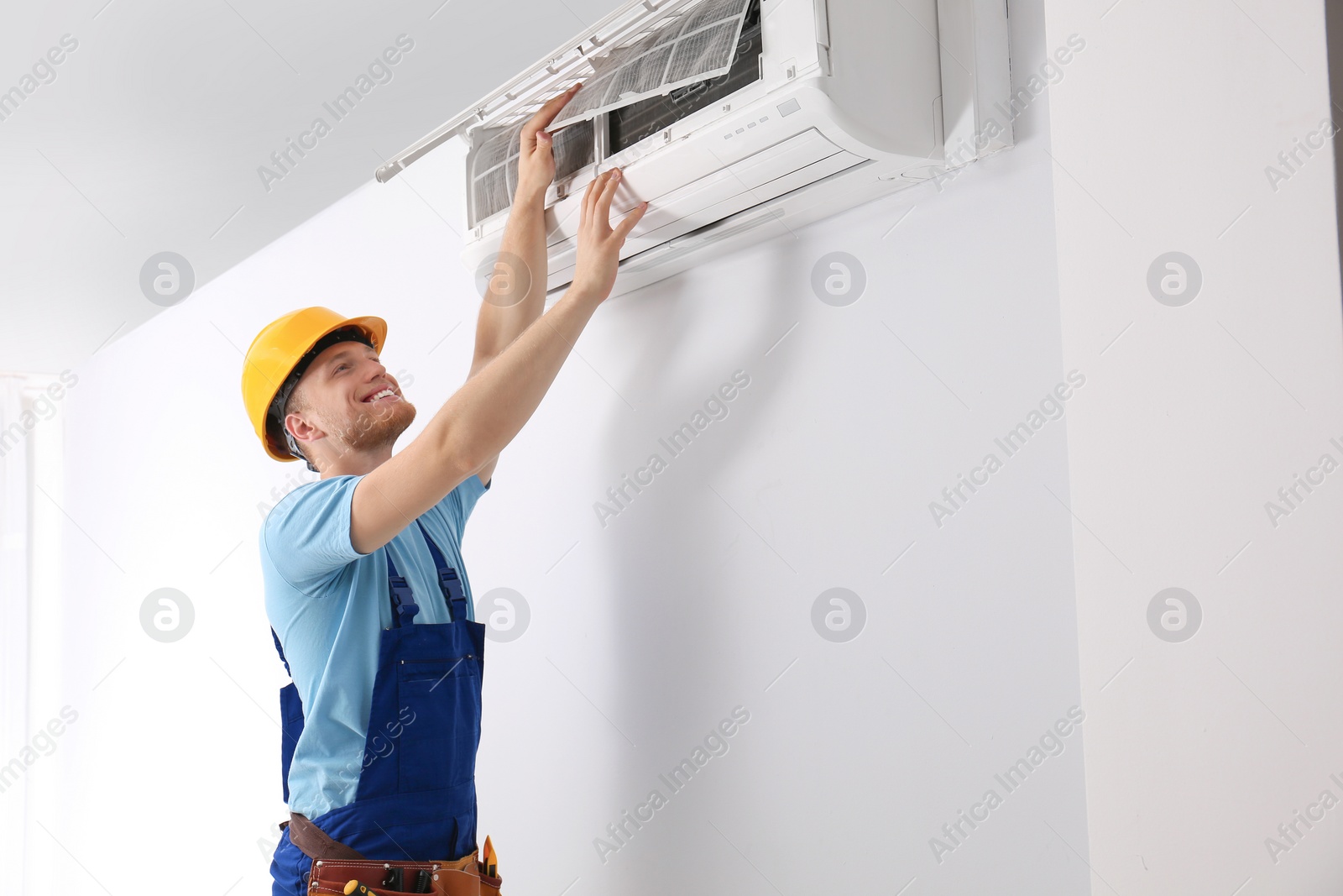 Photo of Professional technician maintaining modern air conditioner indoors