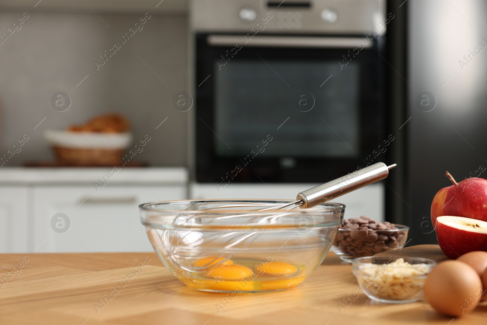 Photo of Cooking process. Metal whisk, bowl and products on wooden table in kitchen, closeup. Space for text