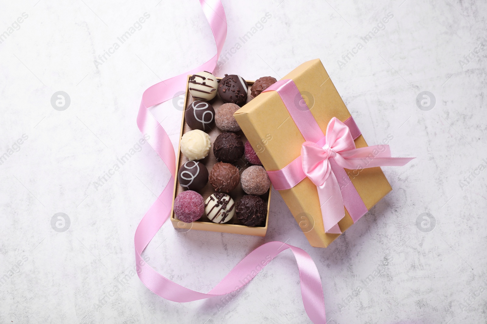 Open box with delicious chocolate candies and pink ribbon on white table, top view Photo of Open box with delicious chocolate candies and pink ribbon on white table, top view