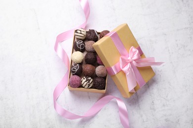 Photo of Open box with delicious chocolate candies and pink ribbon on white table, top view