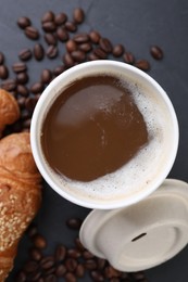 Photo of Coffee to go. Paper cup with tasty drink, croissant and beans on black table, flat lay