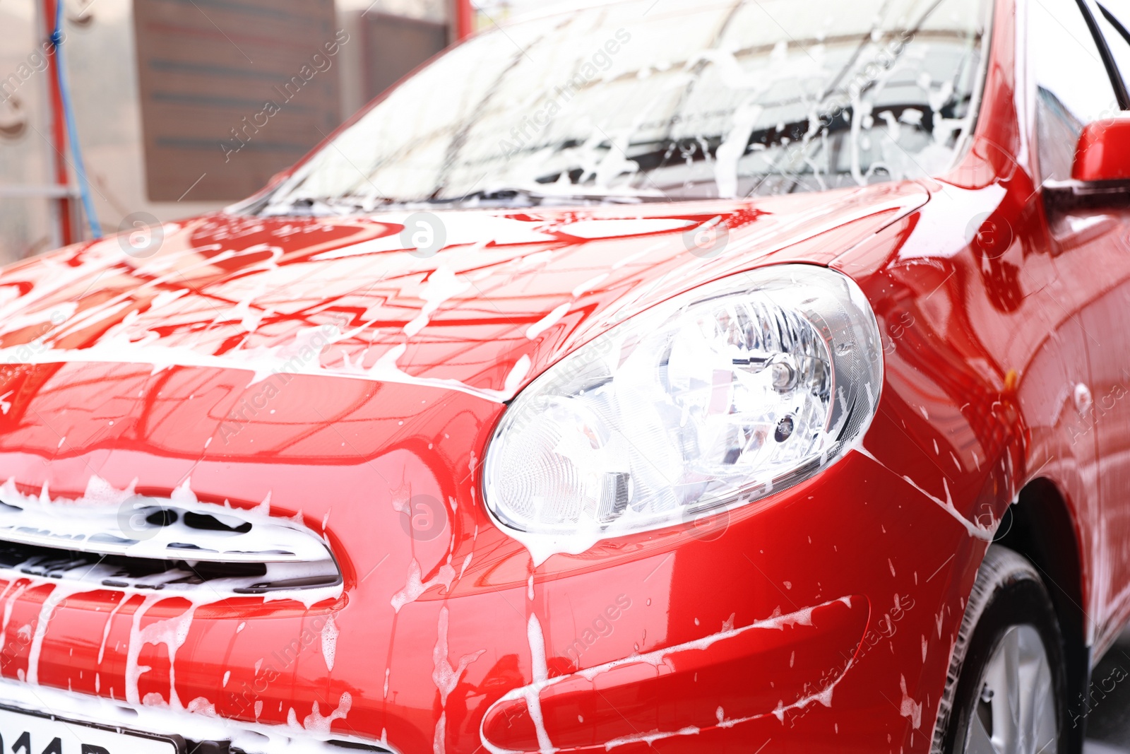 Photo of Red auto with foam at car wash. Cleaning service