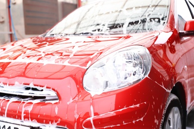 Photo of Red auto with foam at car wash. Cleaning service