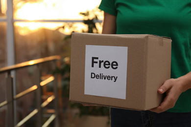 Photo of Courier holding parcel with sticker Free Delivery indoors, closeup